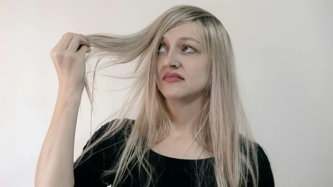 Mujer rubia de pelo largo sujetando una mecha y mirándola con gesto de duda