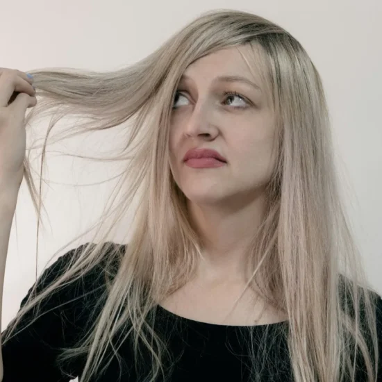 Mujer rubia de pelo largo sujetando una mecha y mirándola con gesto de duda